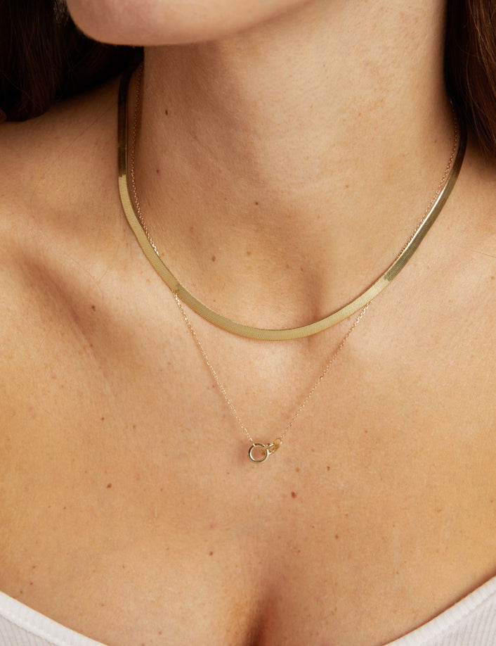 Model. Gold necklace with a small pendant on a person wearing a white top.