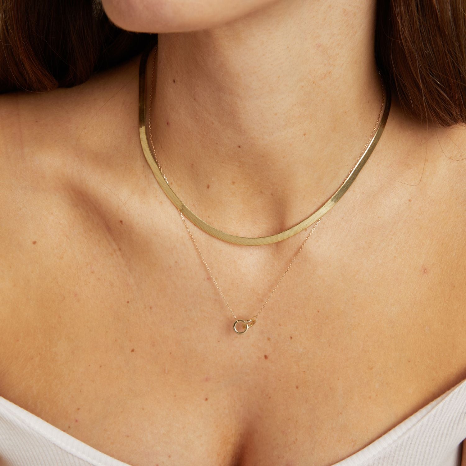 Model. Gold necklace with a small pendant on a person wearing a white top.
