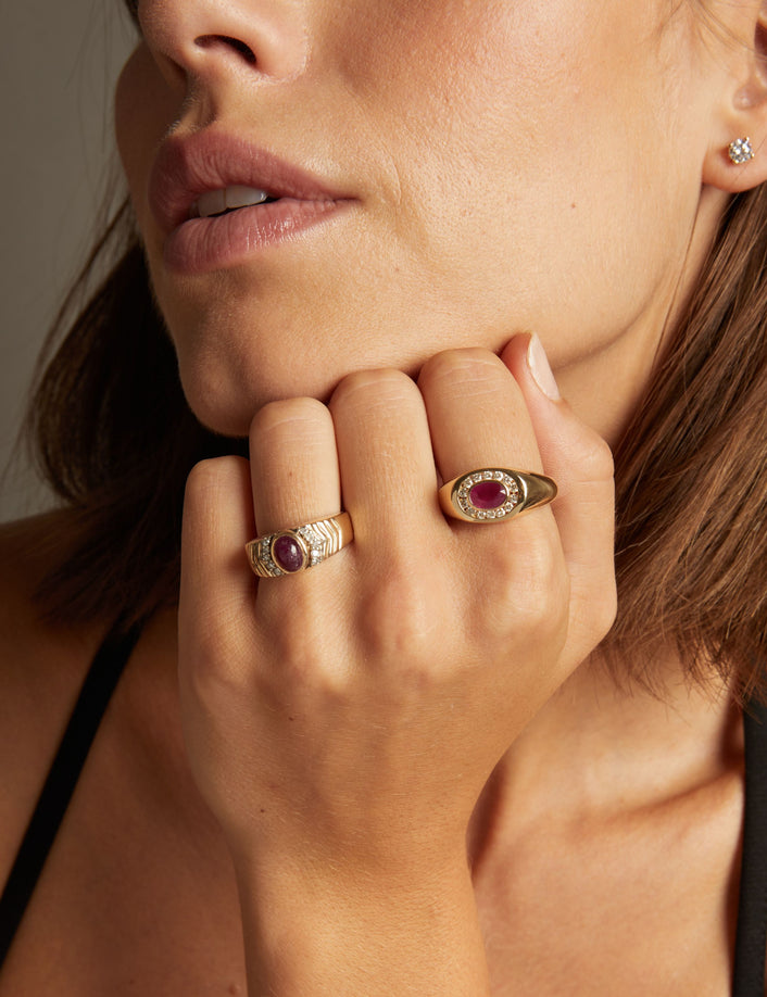 Close up of woman wearing red ruby statement rings on neutral background. 