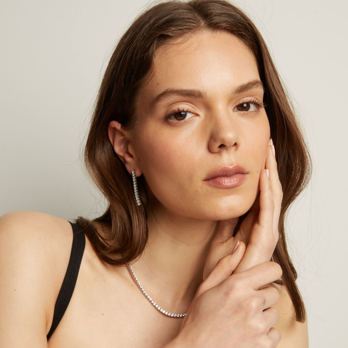 A woman wearing tennis earrings and necklace with a neutral background.