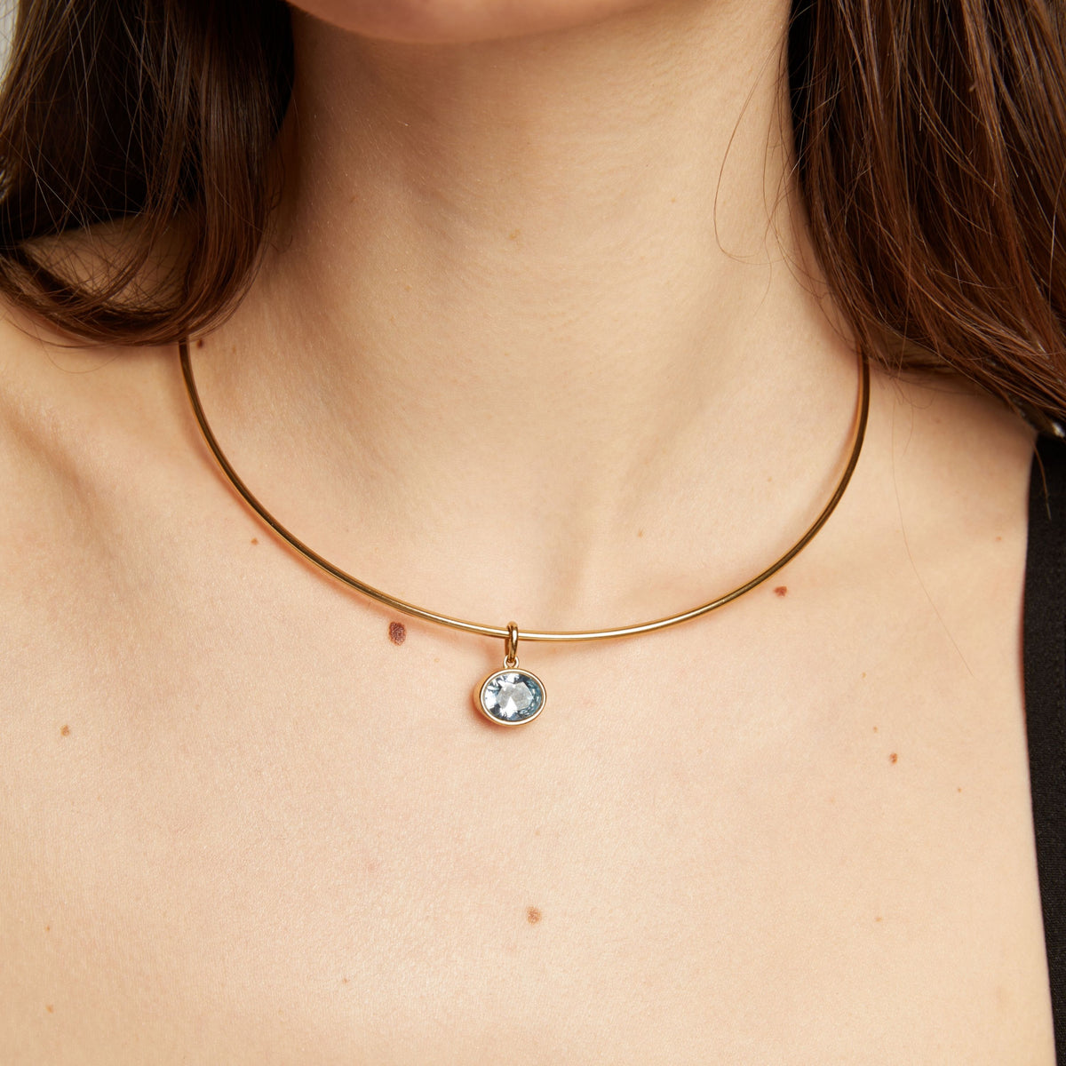 Gold necklace with an aquamarine pendant worn by a woman.