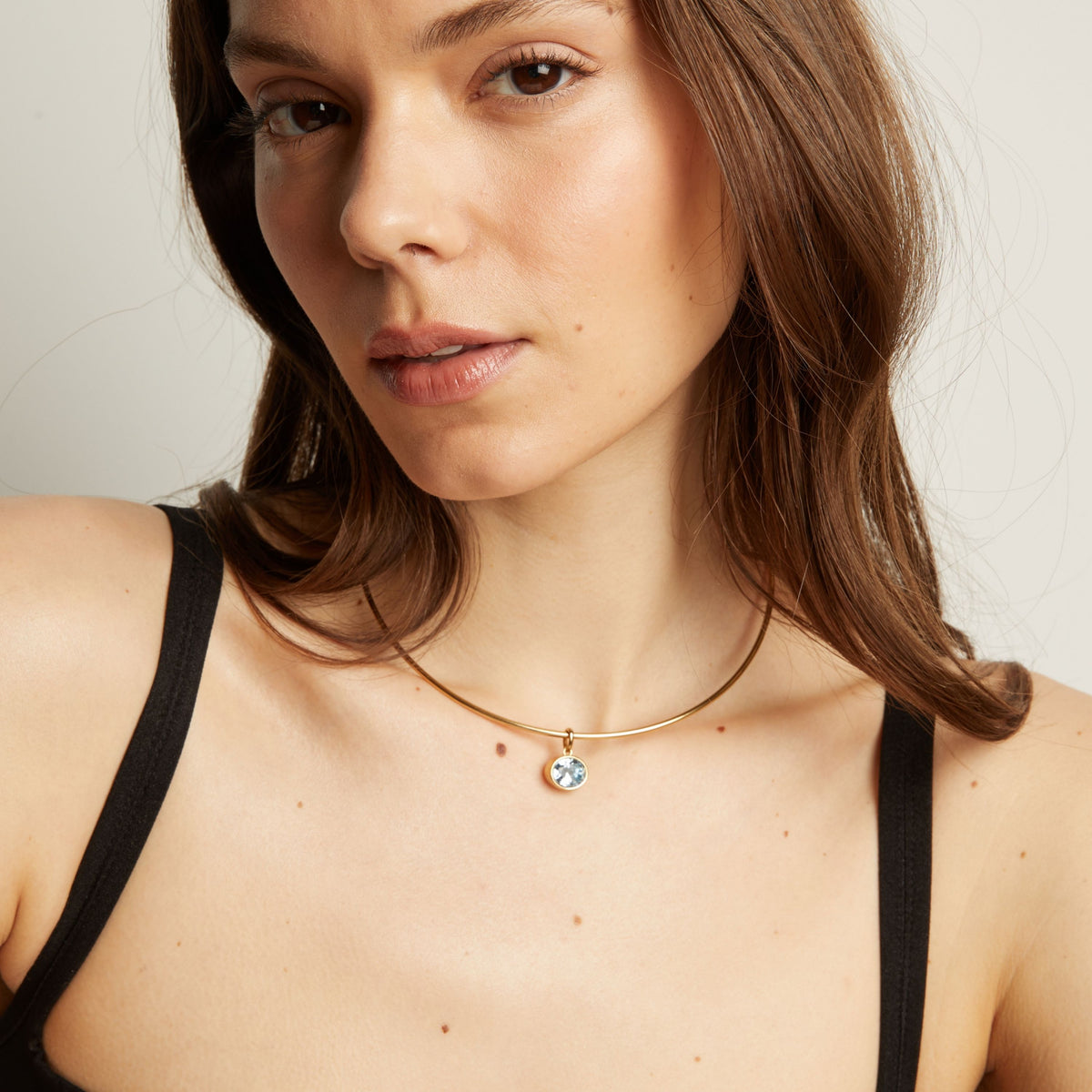 Model. Close up of a woman wearing a gold necklace with an aquamarine pendant.