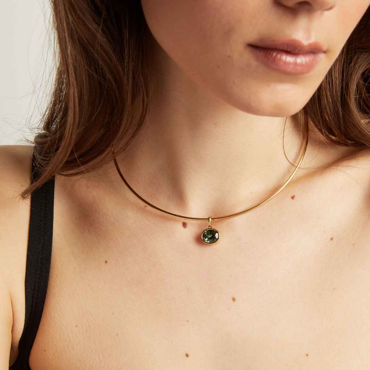 Close up of a woman wearing a gold necklace with a green gemstone pendant.