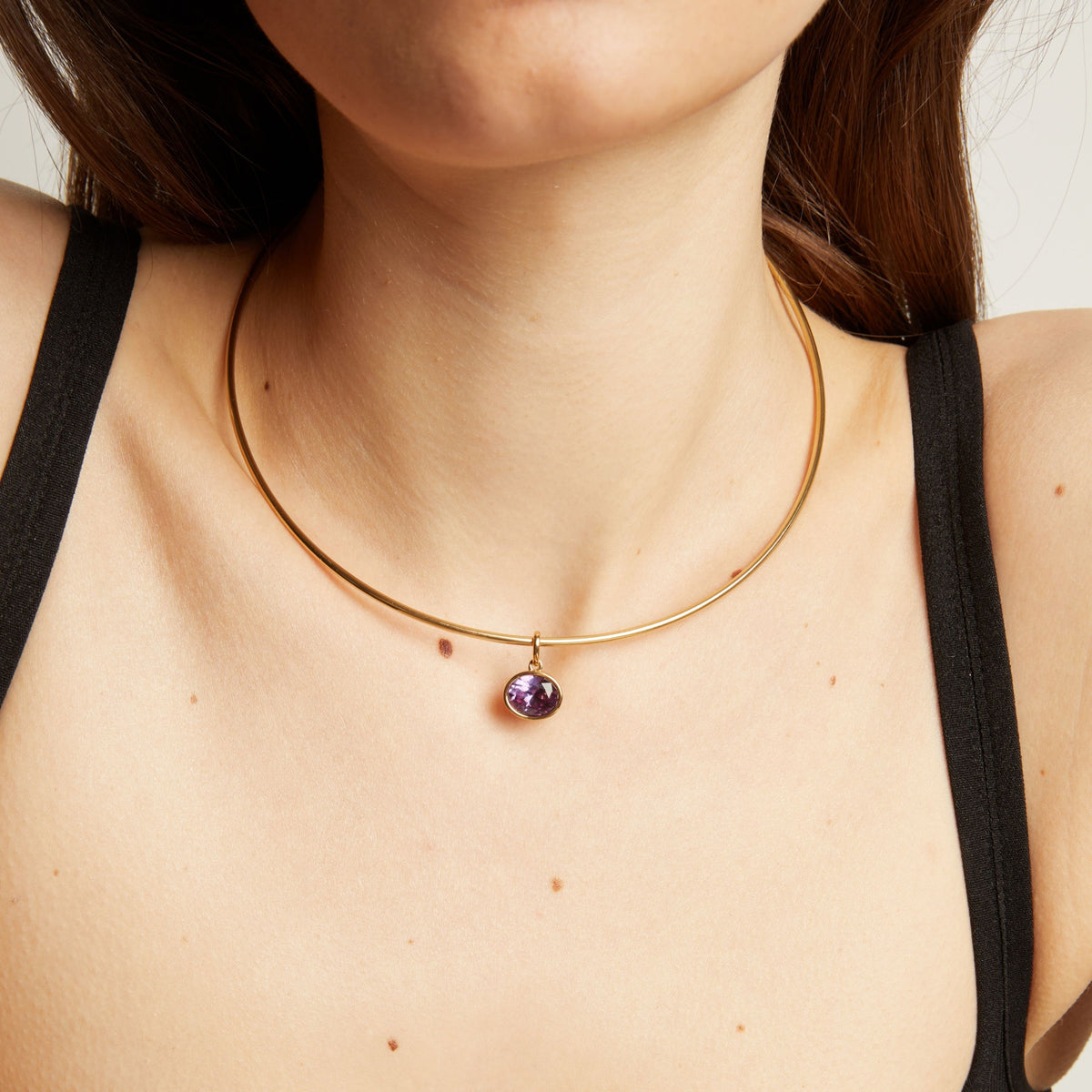 Close up of a woman wearing a gold necklace with an amethyst pendant.