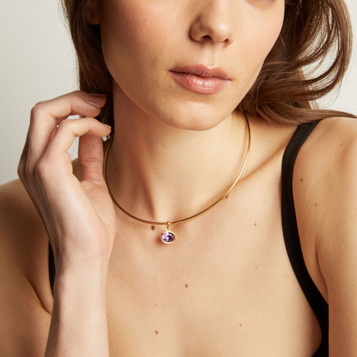  Close up of a woman wearing a gold necklace with an amethyst pendant.