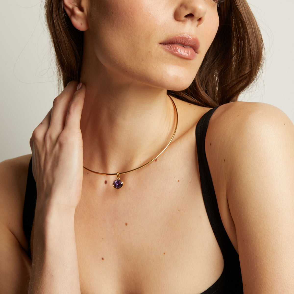 Woman wearing a gold necklace with an amethyst pendant.