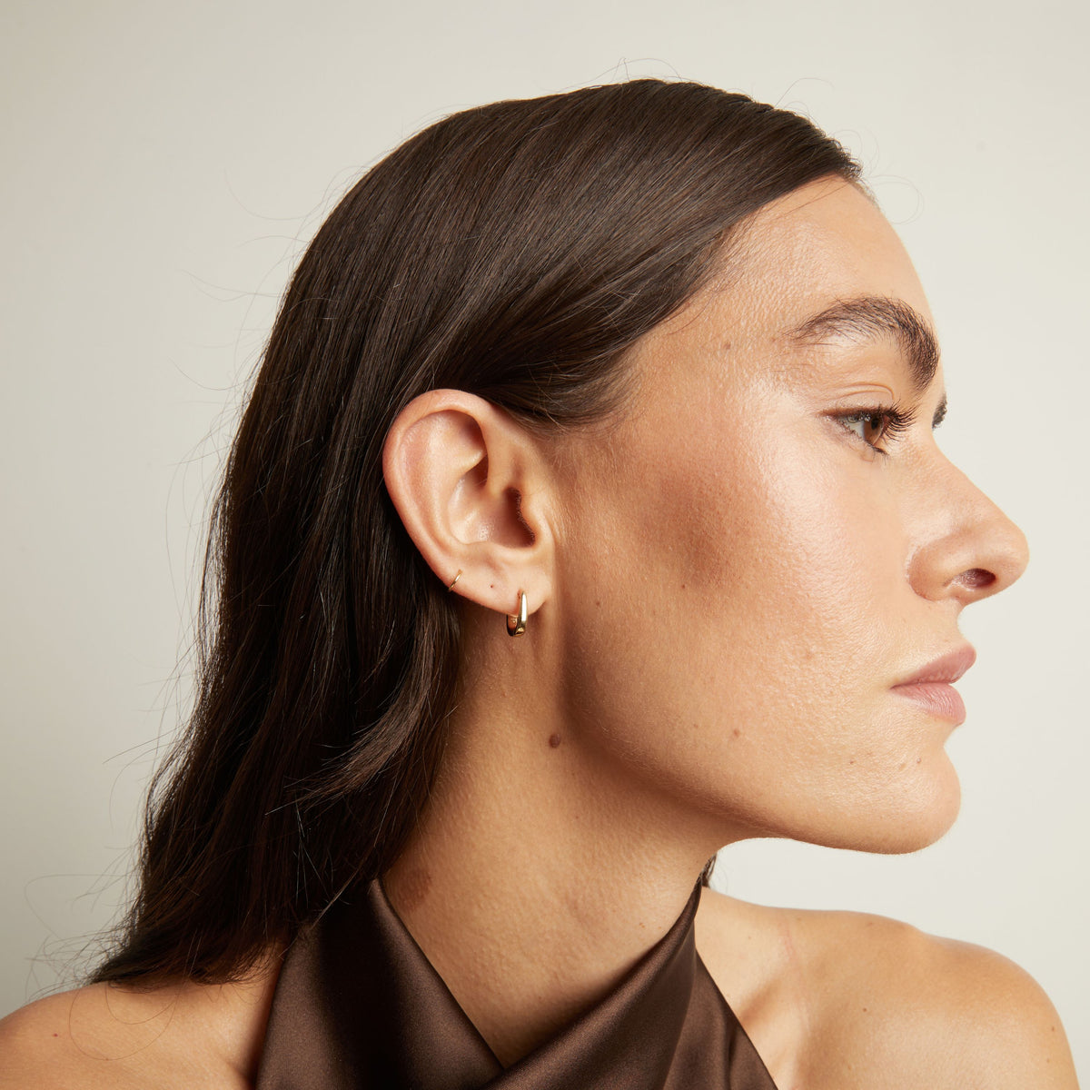 Model. Close up of woman wearing gold huggie earring.
