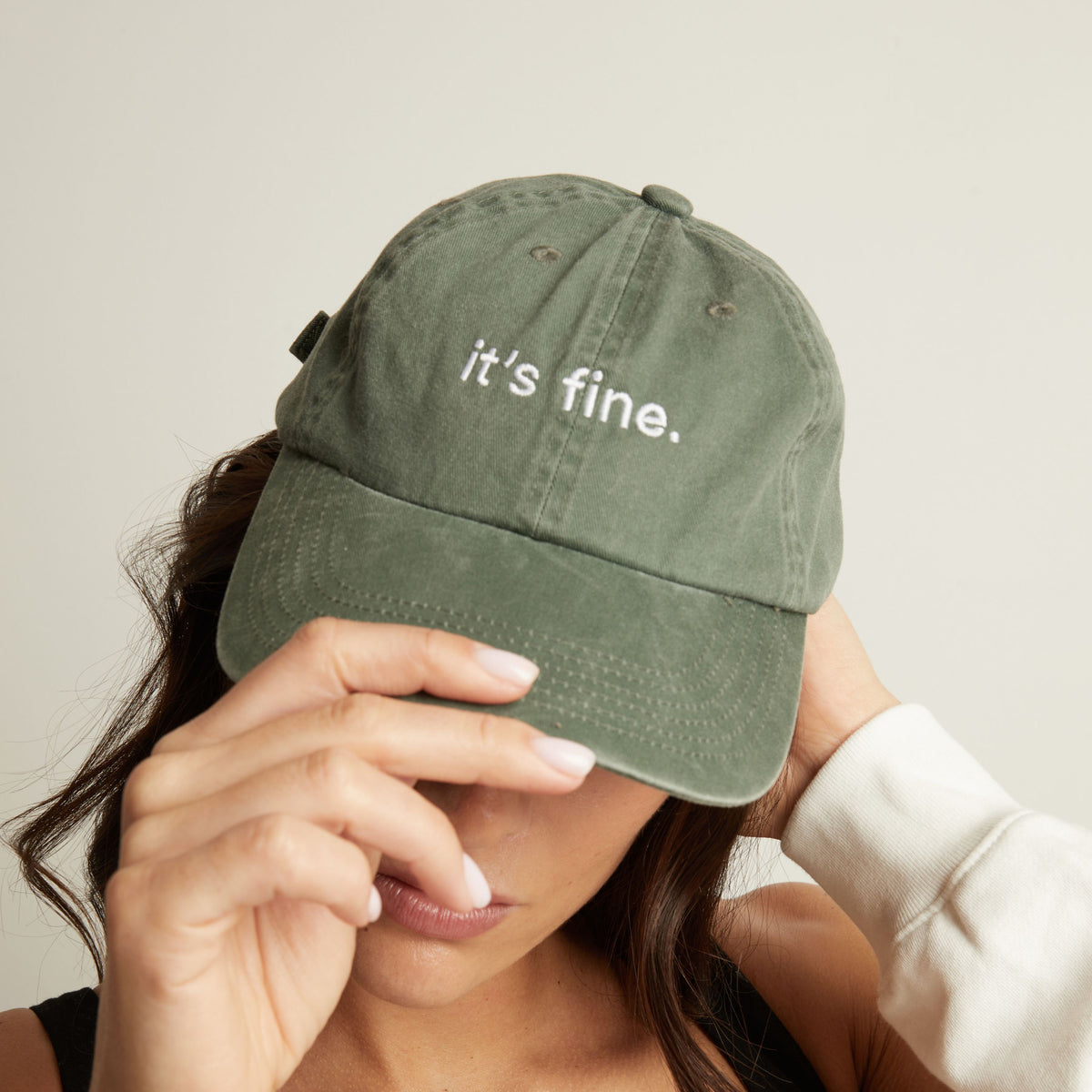 Woman wearing a green cap with 'it's fine' text on a plain background