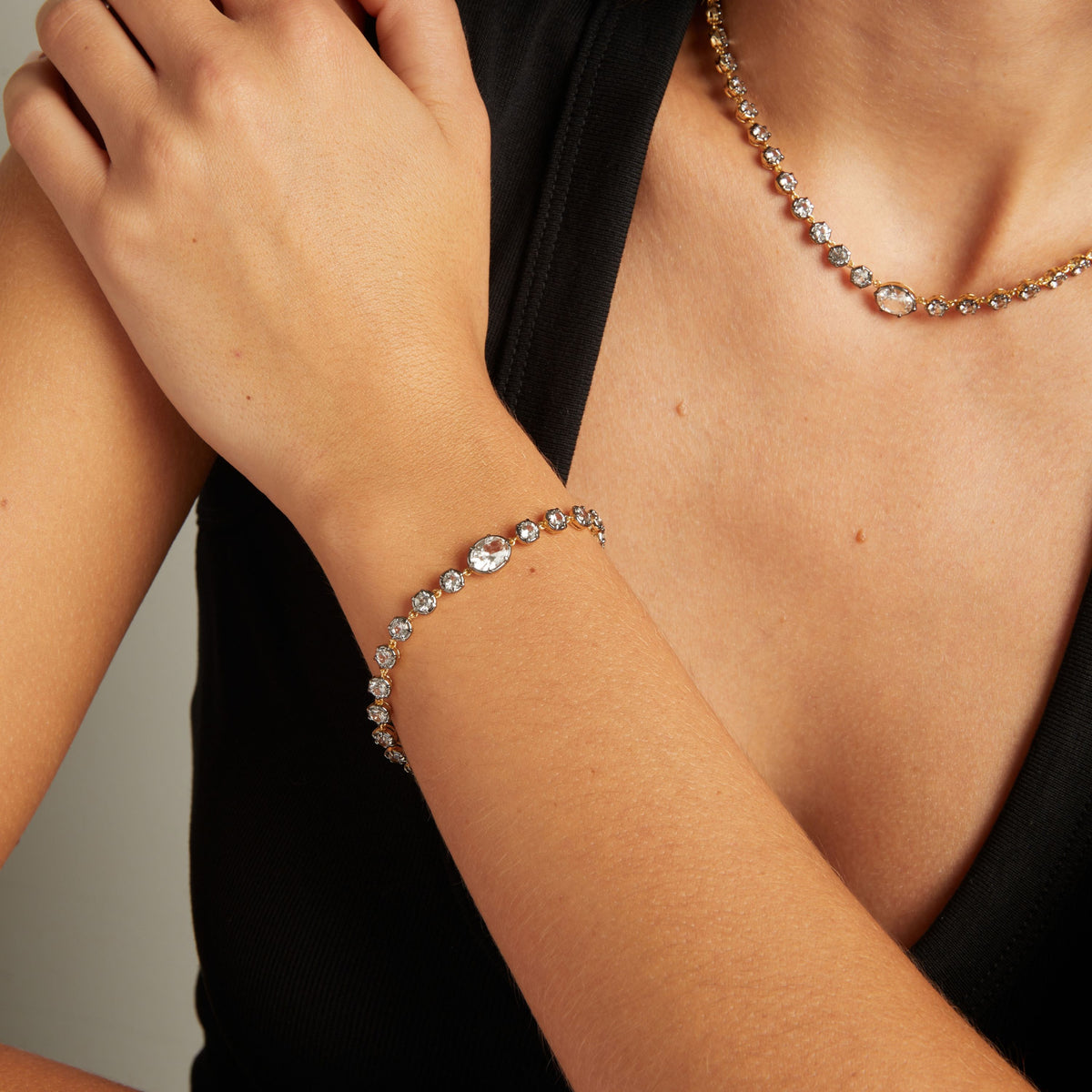 Model. Close up of a woman in a black top wearing a Georgian set tennis bracelet with matching necklace on neutral background.