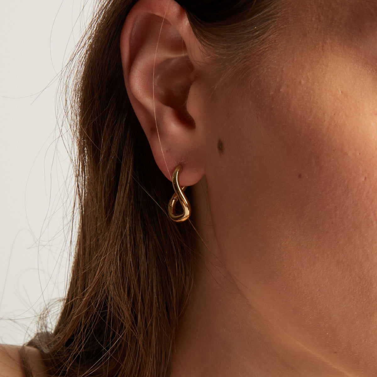 Close up of a woman wearing gold twist earrings with a neutral background.