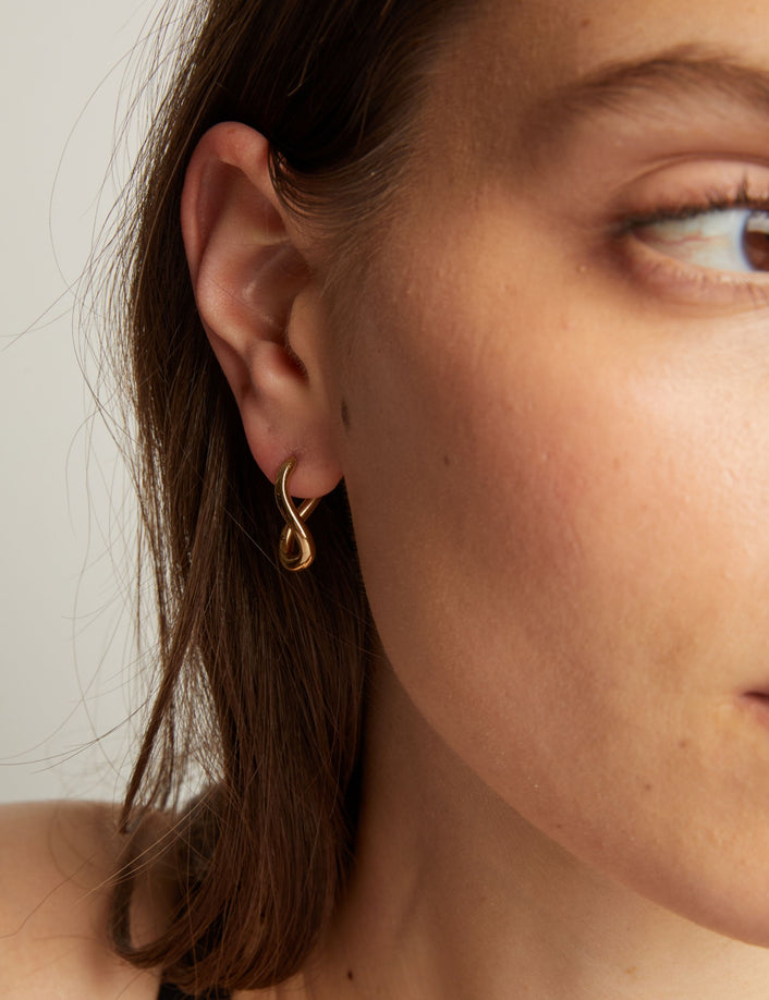 Model. Close up of a woman wearing gold twist earrings with a neutral background.