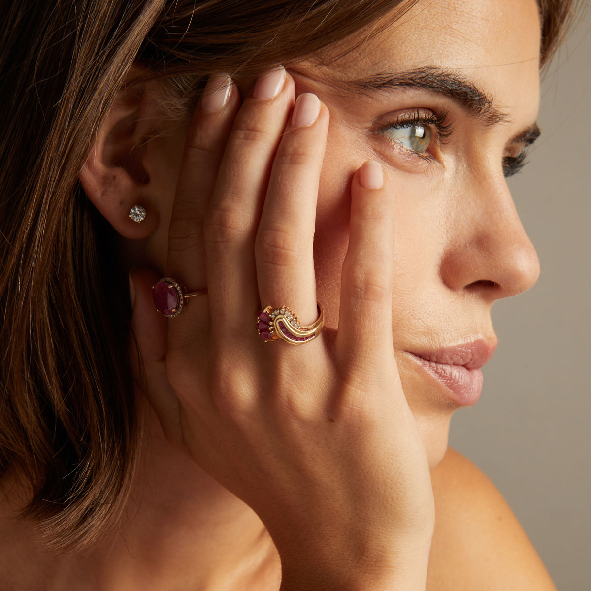 Close up of woman wearing red ruby statement rings on neutral background. 