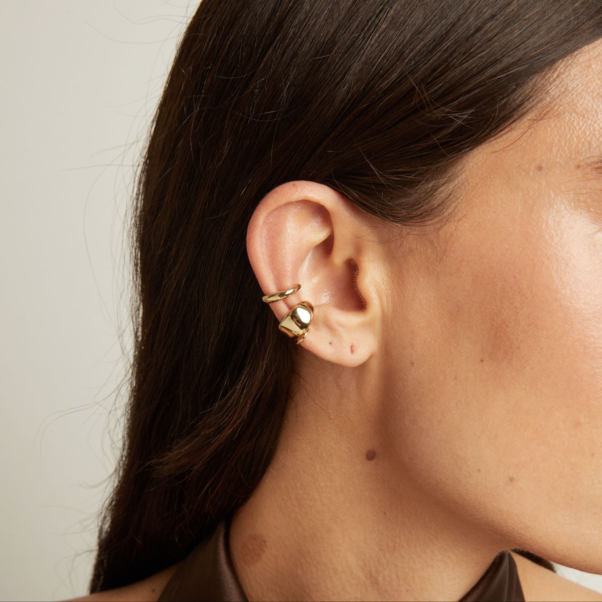 Model. Close up of woman wearing two gold ear cuffs. 