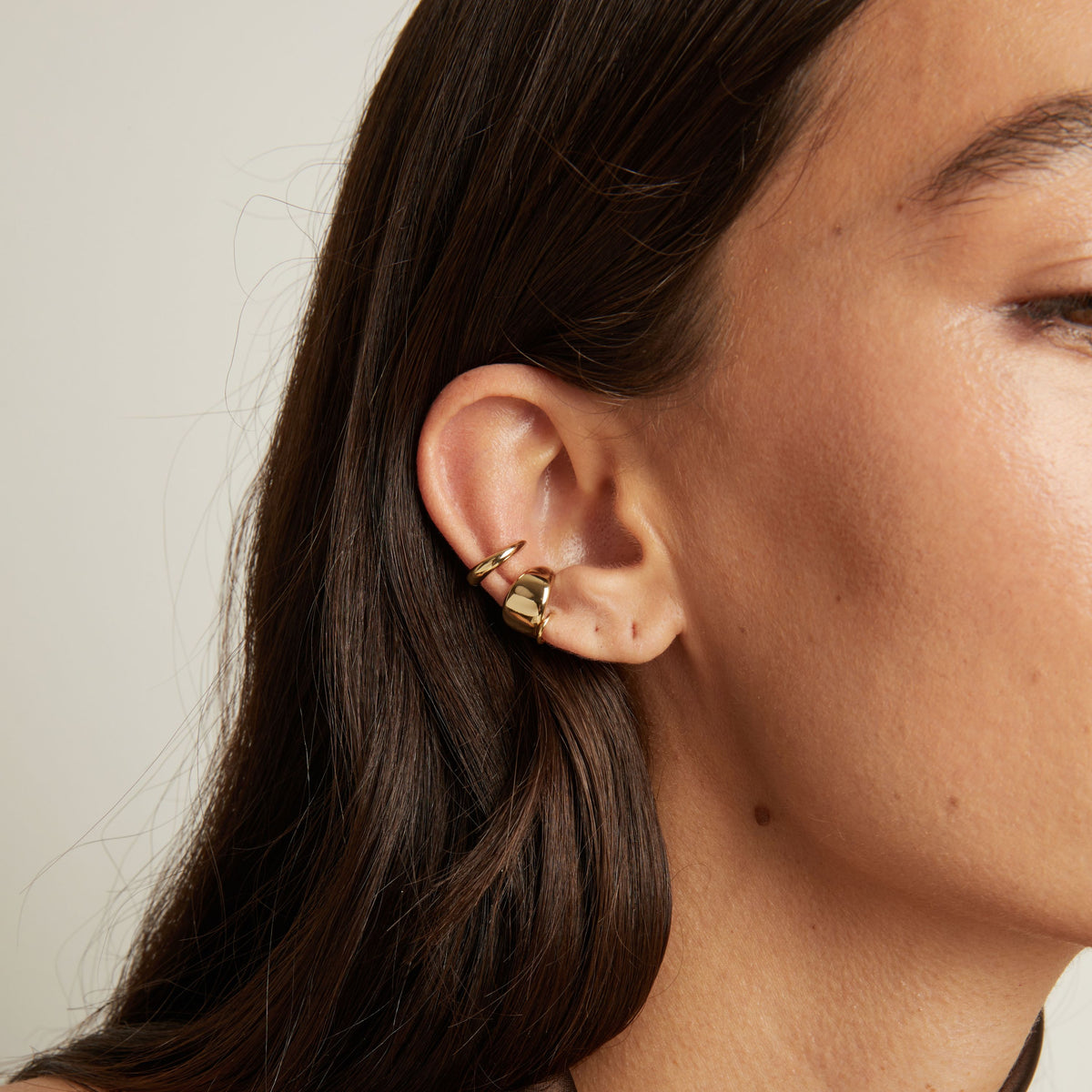 Close up of woman wearing two gold ear cuffs. 