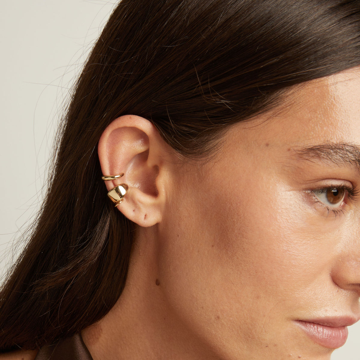Close up of woman wearing two gold ear cuffs. 