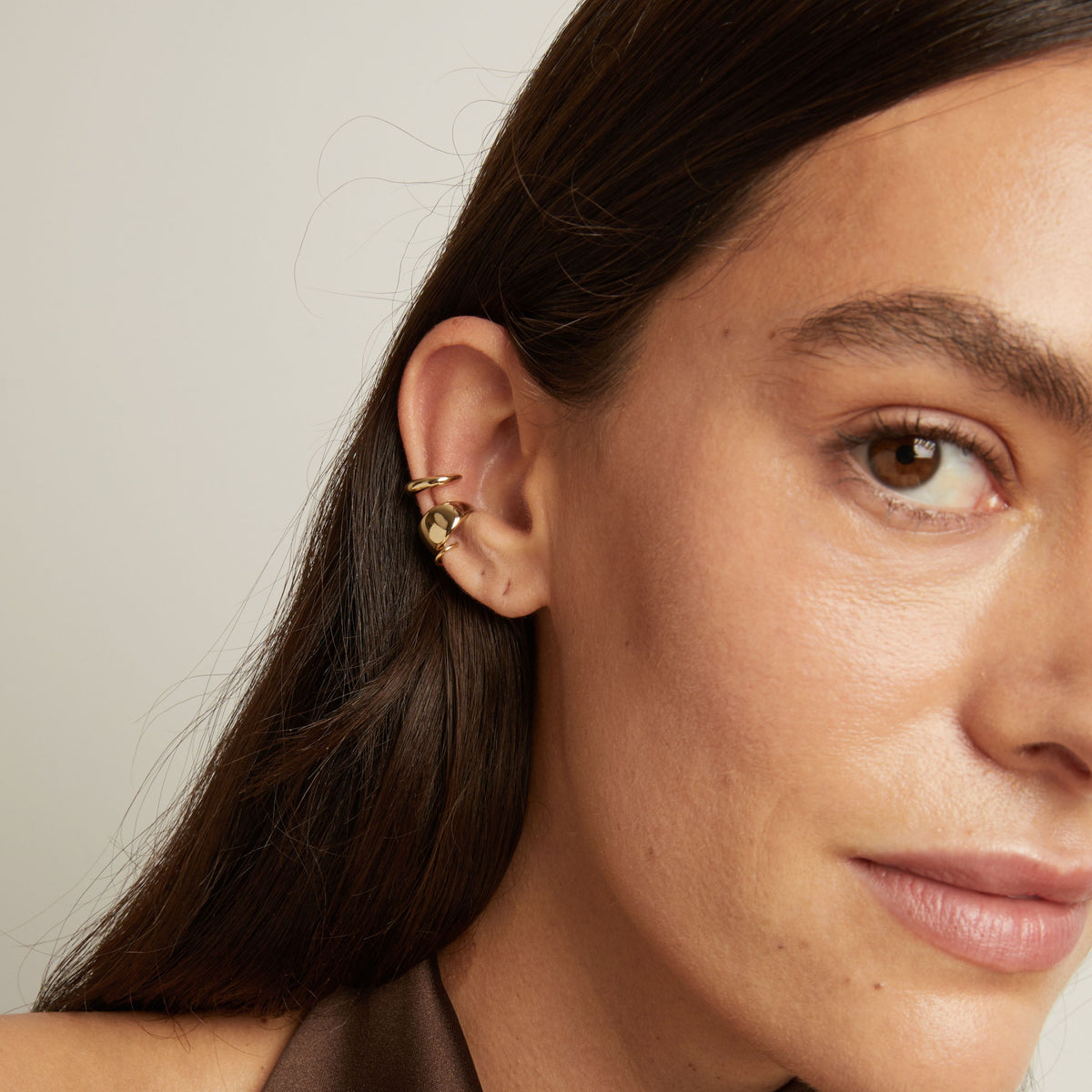Model. Close up of woman wearing two gold ear cuffs. 