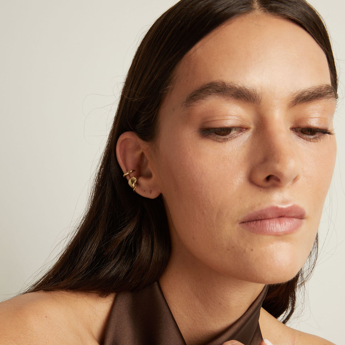 Close up of woman wearing two gold ear cuffs. 