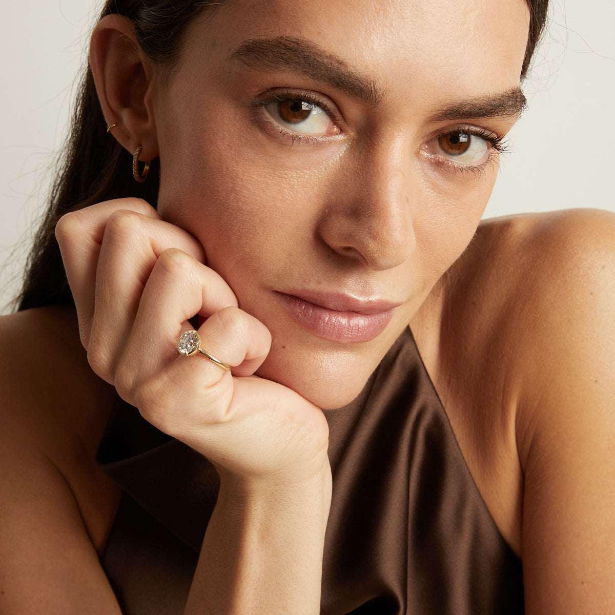 Model. A close-up lifestyle shot of a woman wearing a delicate gold ring with a round diamond. 