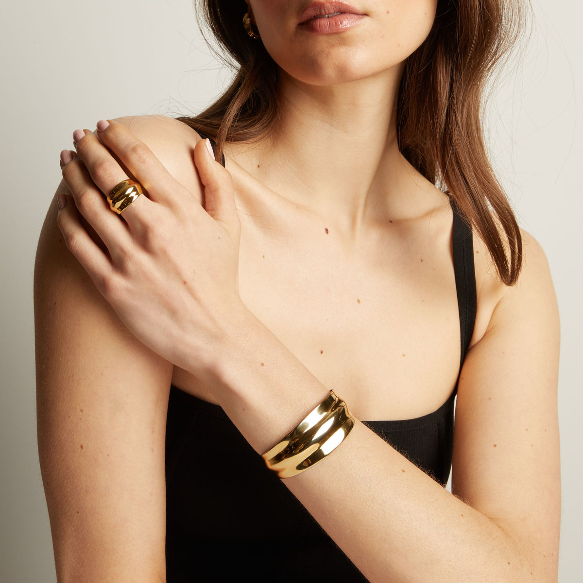 Woman wearing a gold bracelet and ring on a neutral background