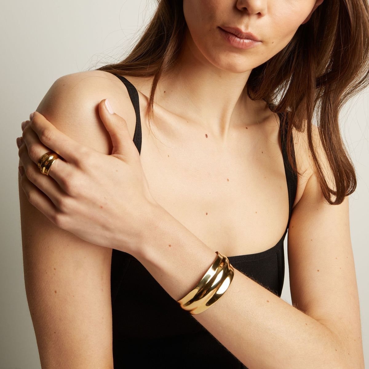 Model. Woman wearing a gold bracelet and ring on a neutral background
