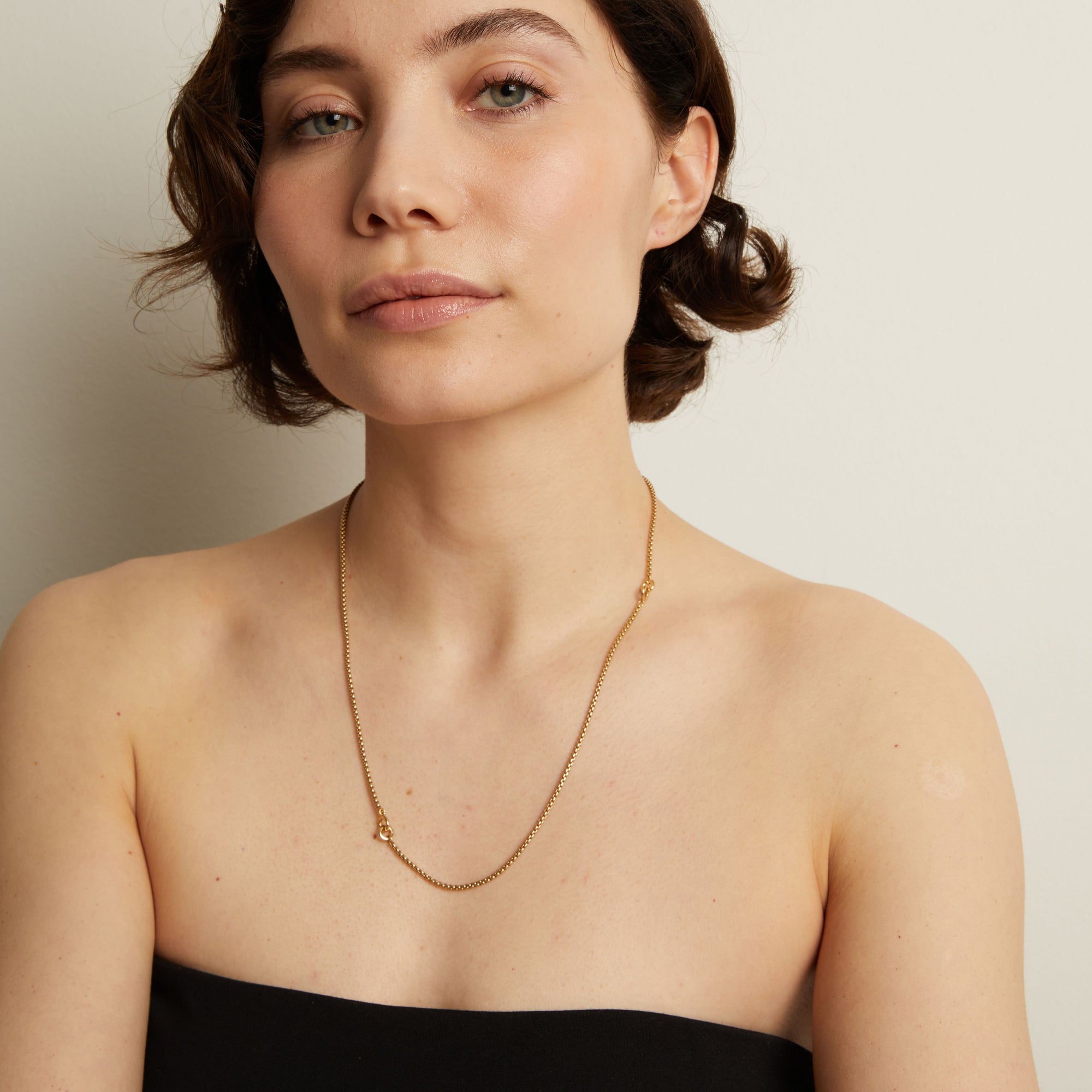 Woman wearing a gold necklace against a plain background