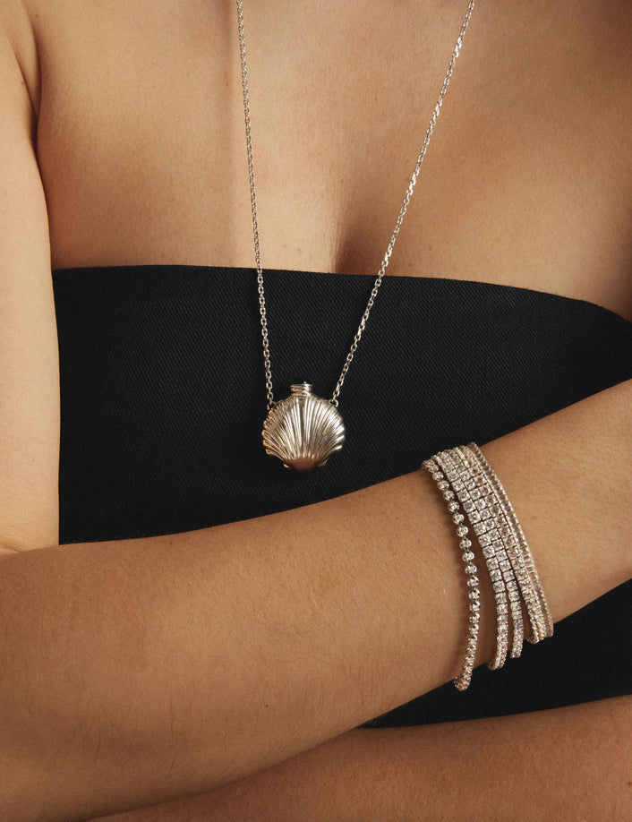 Model. Woman wearing a black strapless top with stacked diamond tennis bracelets and a shell shaped necklace