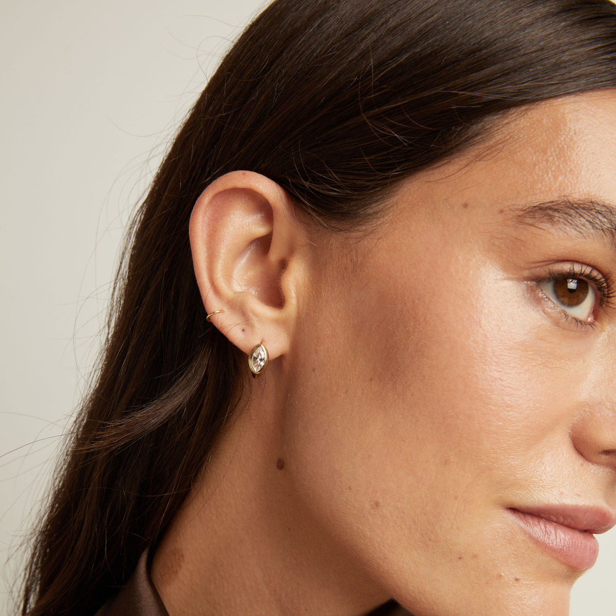 Close up of woman wearing a gold bezel huggie earring on neutral background.