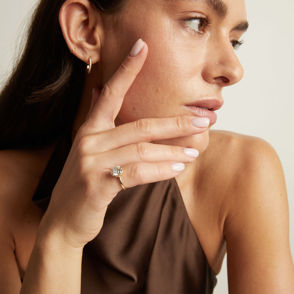 A close-up lifestyle shot of a woman wearing a delicate gold ring with a round diamond. 
