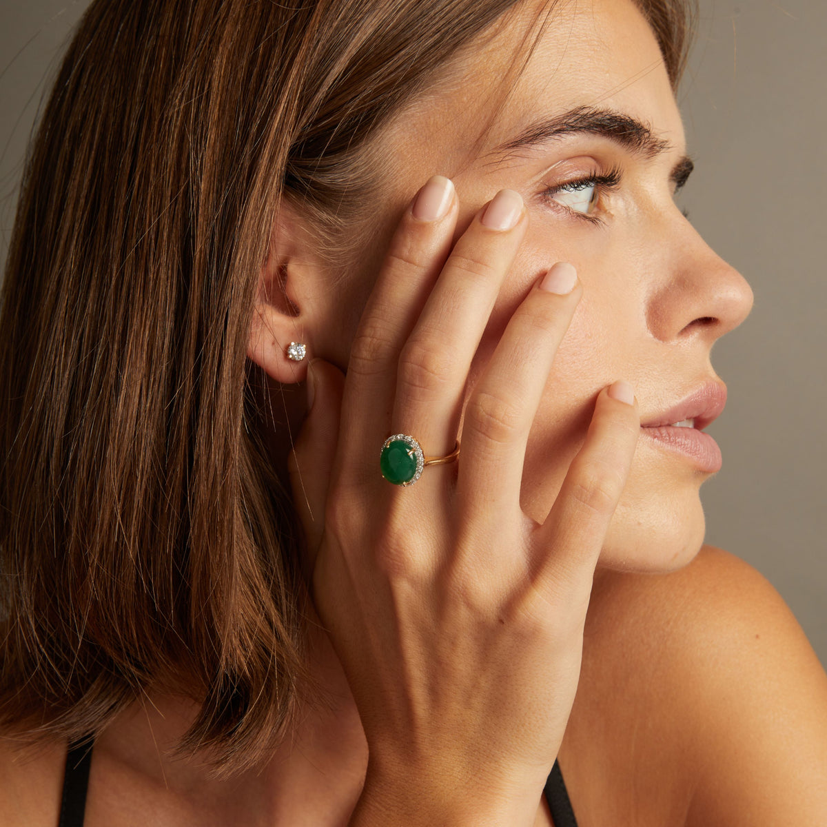 Model. Close up of woman wearing bold green ring on neutral background.
