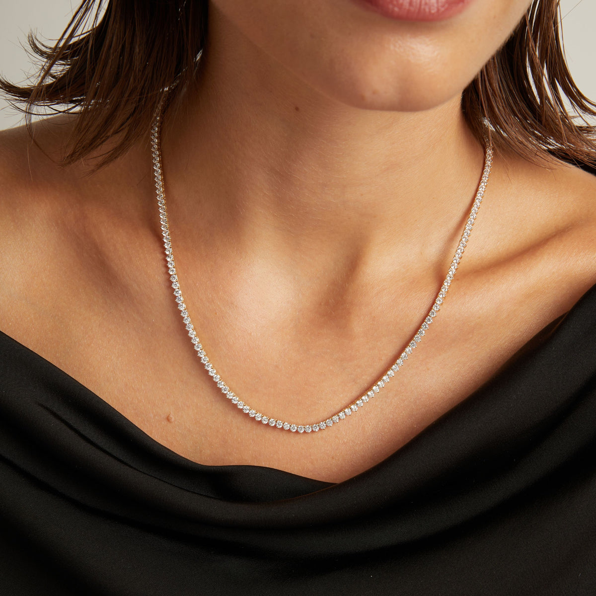 Model. Close up of a woman in a black top wearing a diamond tennis necklace on beige background.