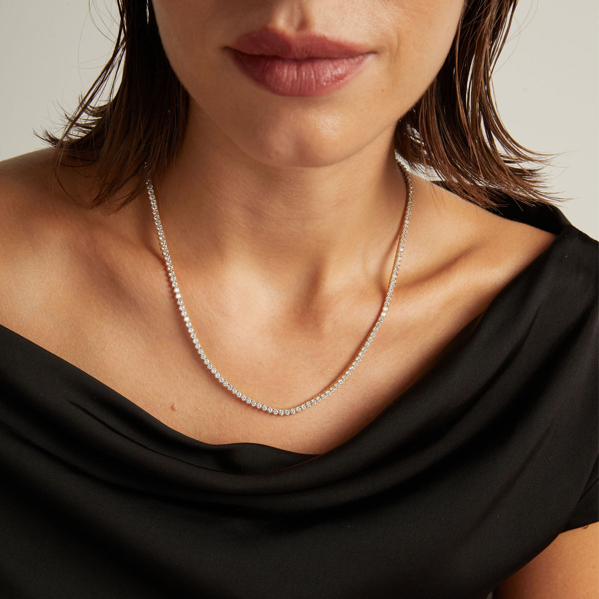 Model. Close up of a woman in a black top wearing a diamond tennis necklace on beige background.