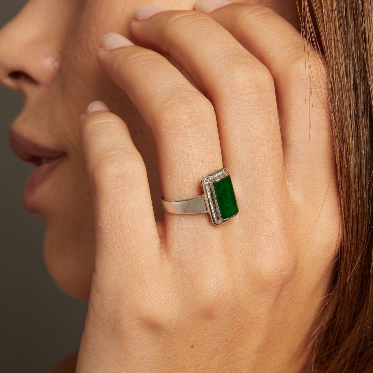 Model. Close up of woman wearing bold green ring on neutral background.
