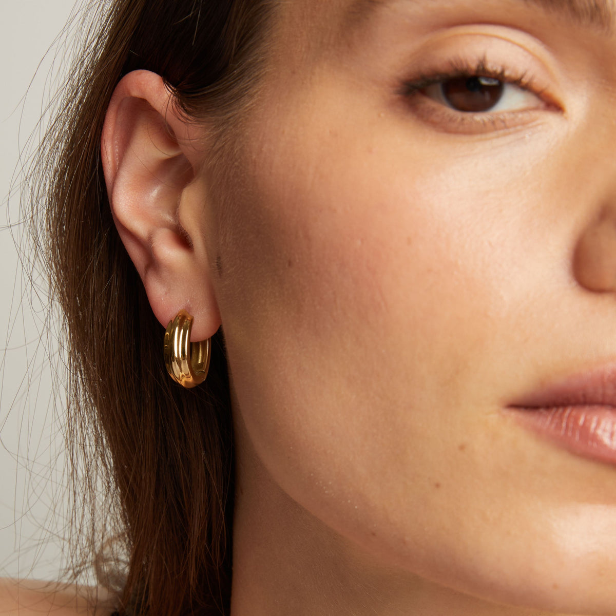 Close up of a person wearing gold hoop earrings with a neutral background