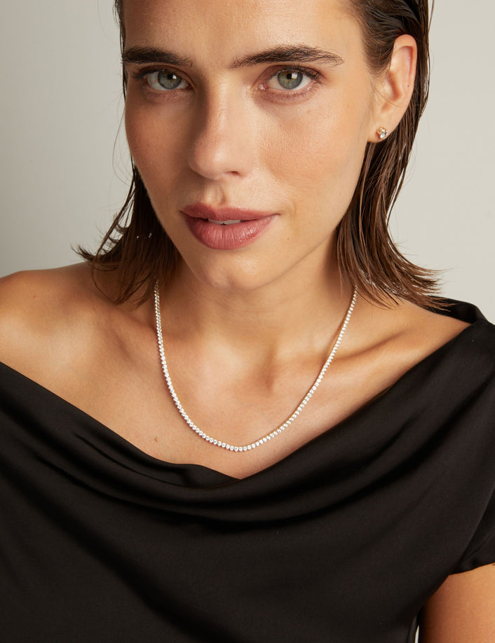Model. Close up of a woman in a black top wearing a diamond tennis necklace on beige background.