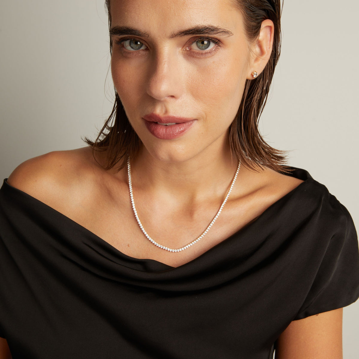 Model. Close up of a woman in a black top wearing a diamond tennis necklace on beige background.