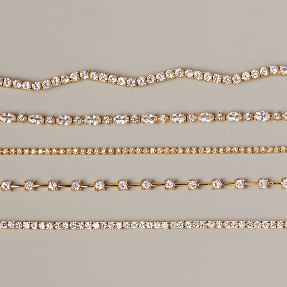 Model. Five different styles of gold diamond tennis necklaces arranged horizontally on a neutral beige background.