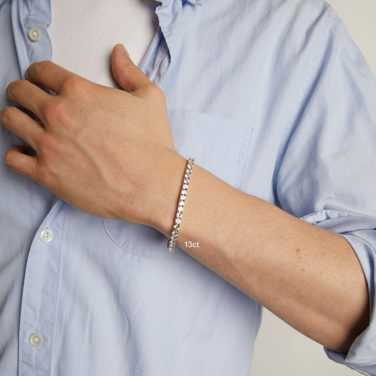 Model. A close-up of a man's wrist wearing a delicate tennis bracelet, shown against a light blue button-down shirt.