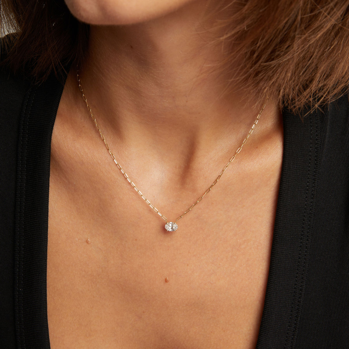 Model. Close up of a woman in a black top wearing a chain necklace with a solitaire oval diamond on neutral background.