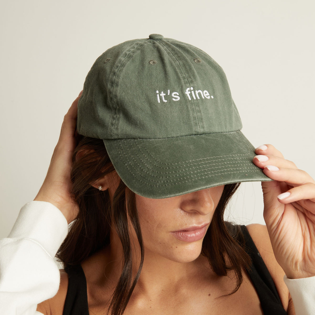 Woman wearing a green cap with 'it's fine' text on a plain background