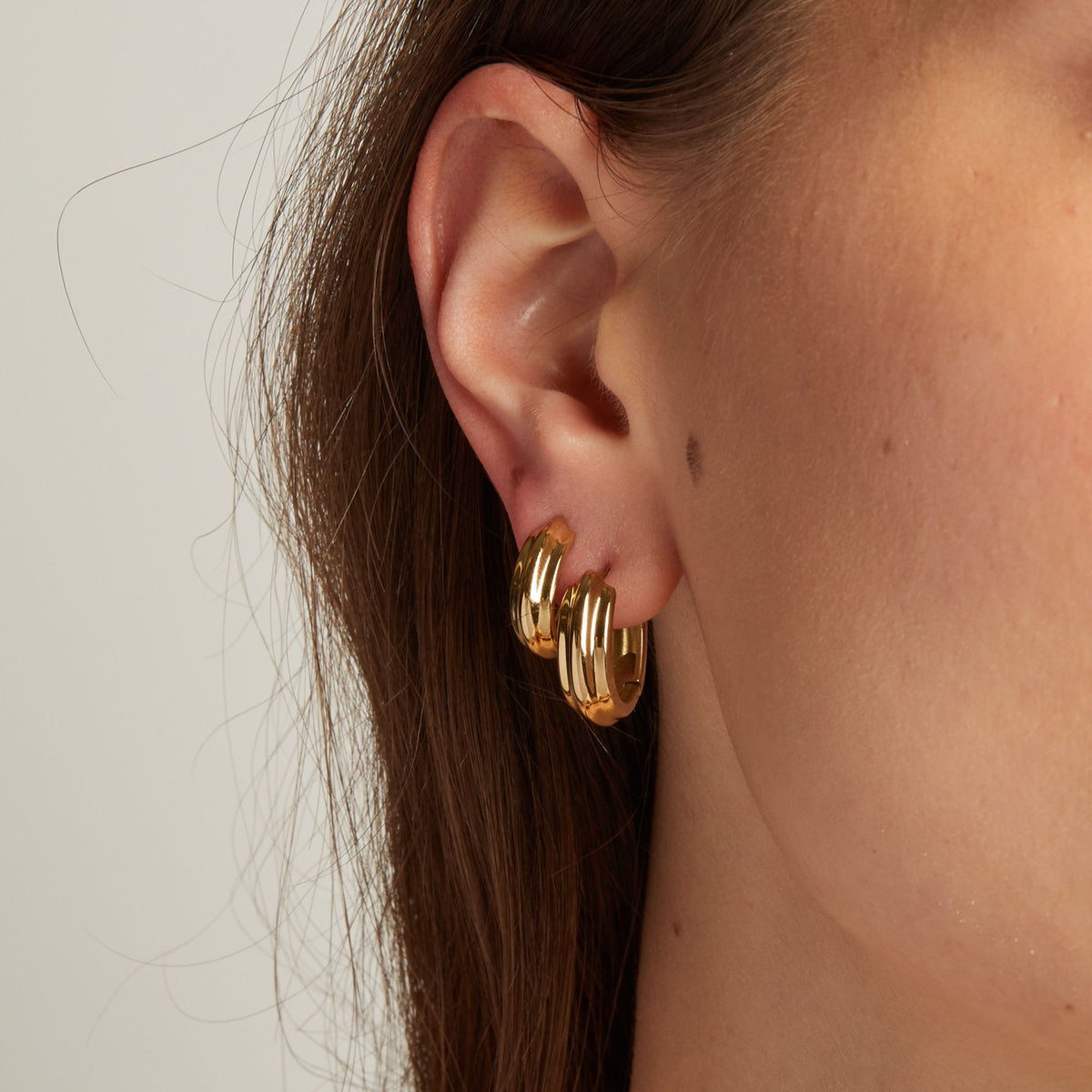 Close up of a woman wearing gold hoop earrings against a neutral background