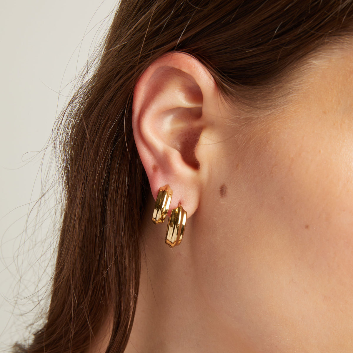 Close up of a person wearing gold hoop earrings with a neutral background