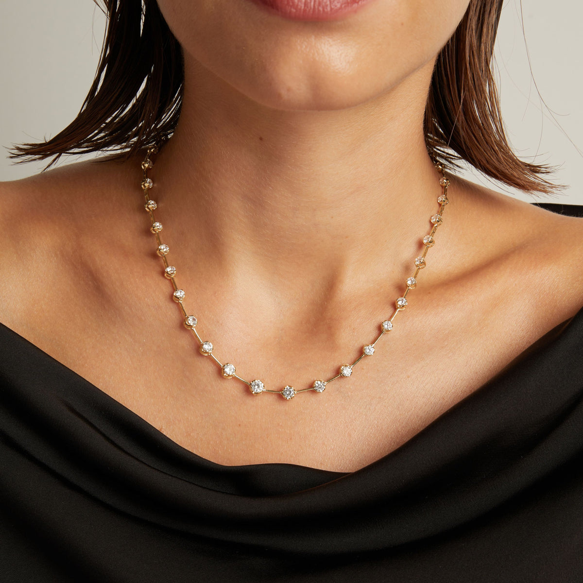 Model. Close up of a woman in a black top wearing a diamond bar necklace on beige background.
