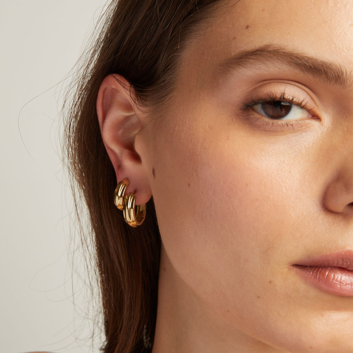 Close up of a woman wearing gold hoop earrings against a neutral background