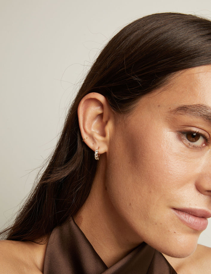 Close up of woman wearing a white sapphire huggie earring on a neutral background.