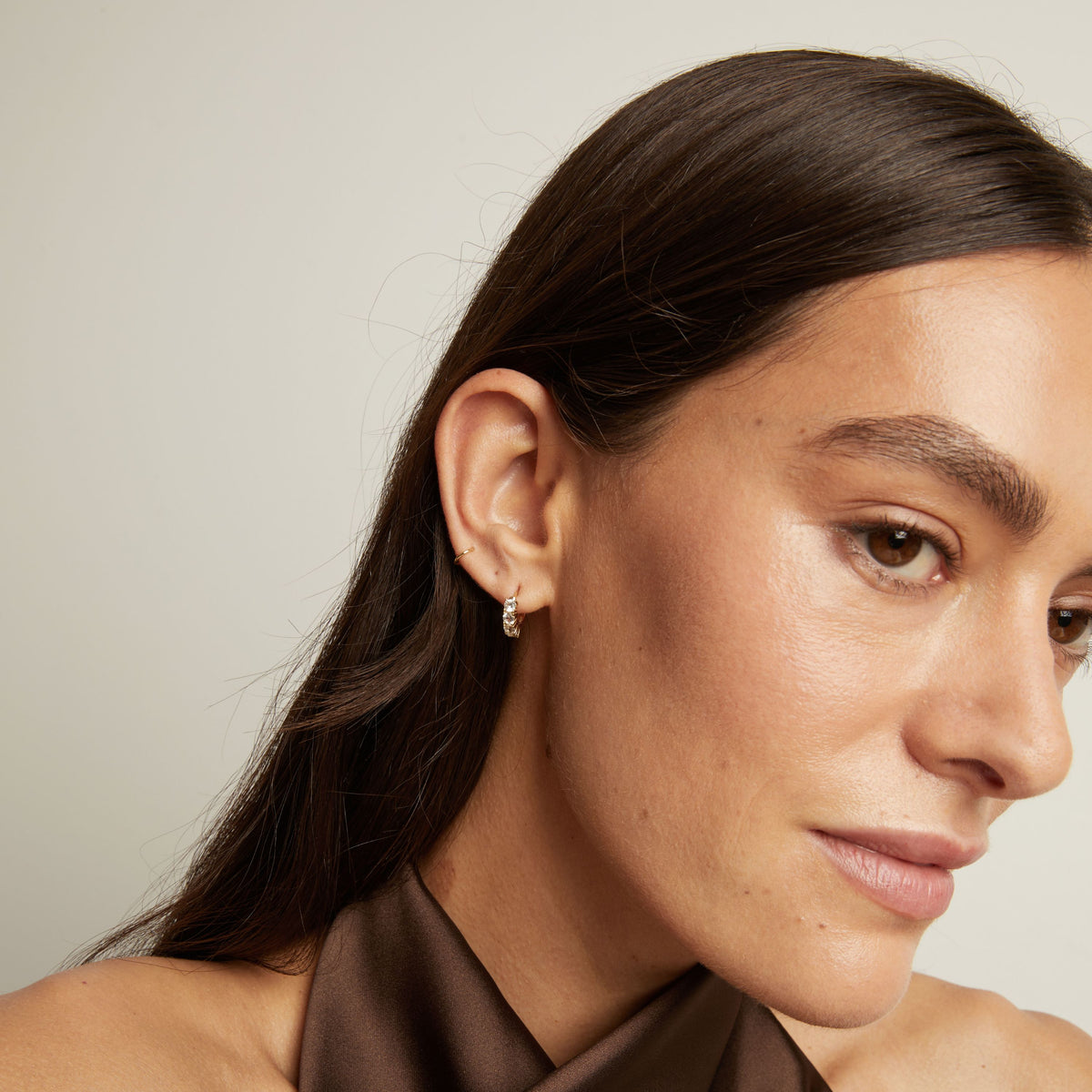 Close up of woman wearing a white sapphire huggie earring on a neutral background.
