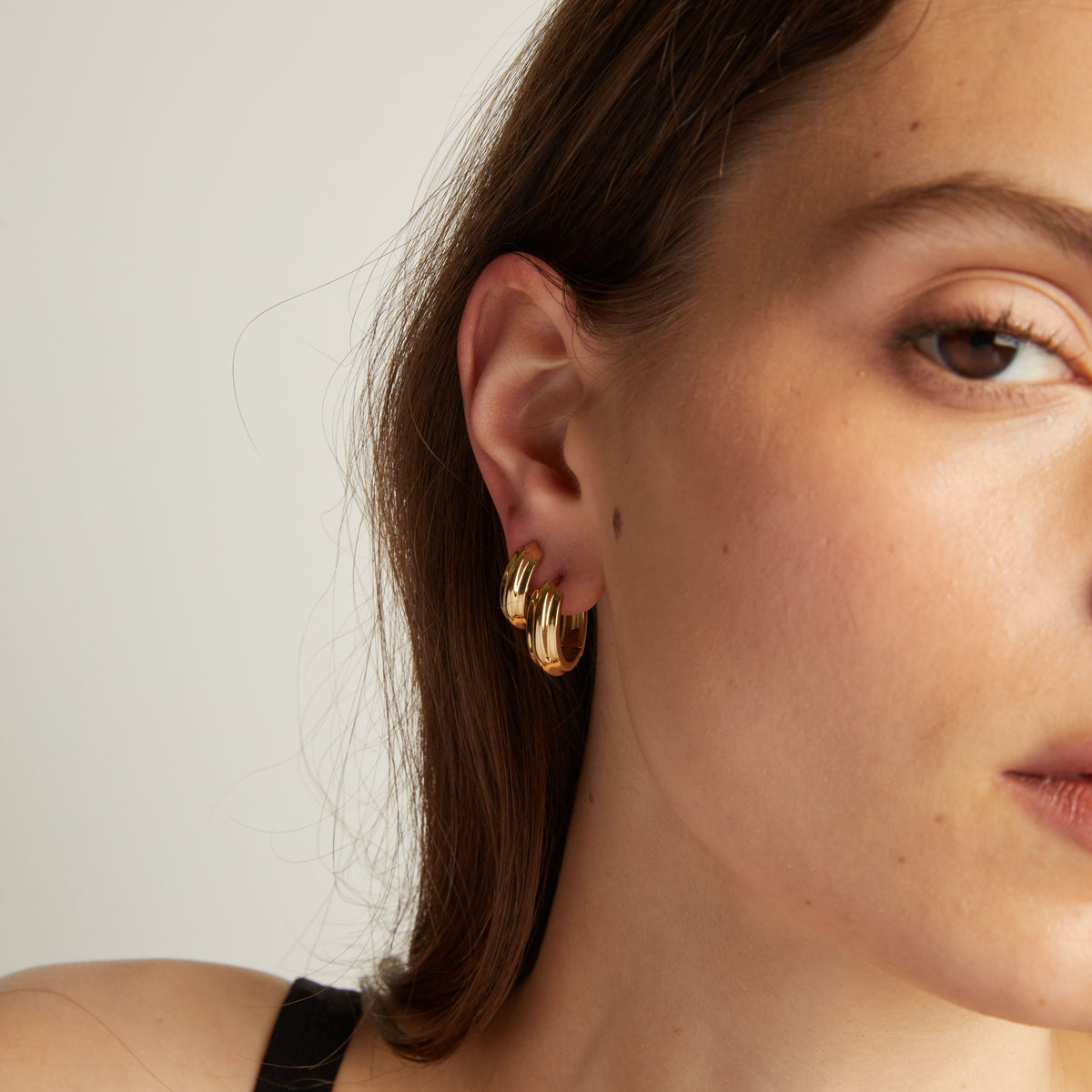 Close up of a woman wearing gold hoop earrings against a neutral background
