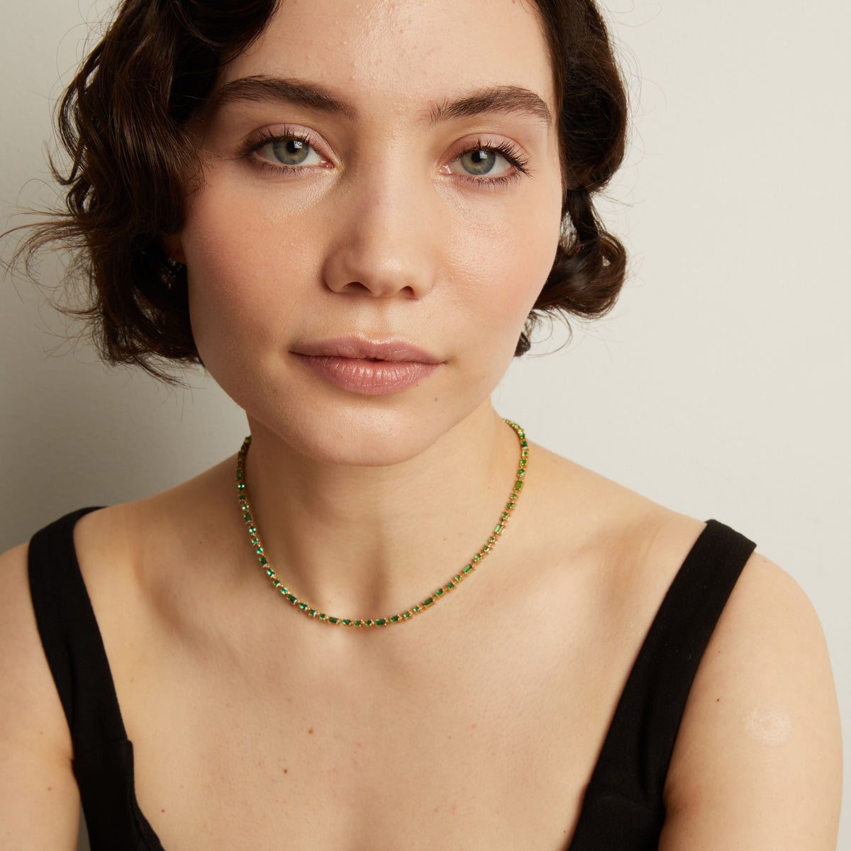 Woman wearing a green tennis necklace against a neutral background. 