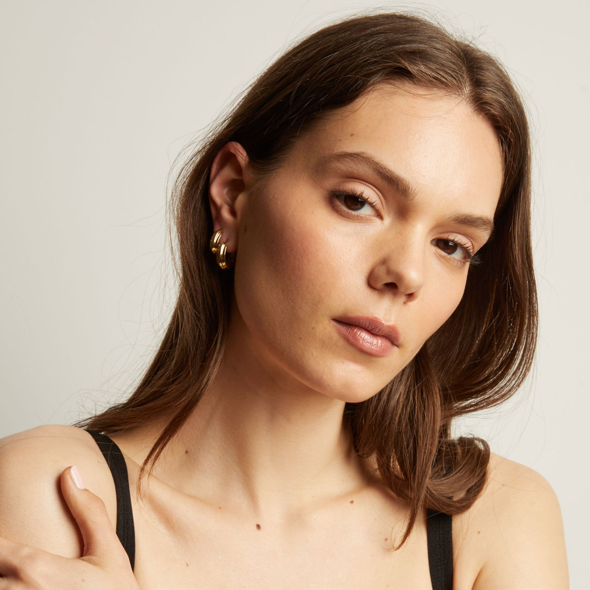 Model. Close up of a person wearing gold hoop earrings with a neutral background