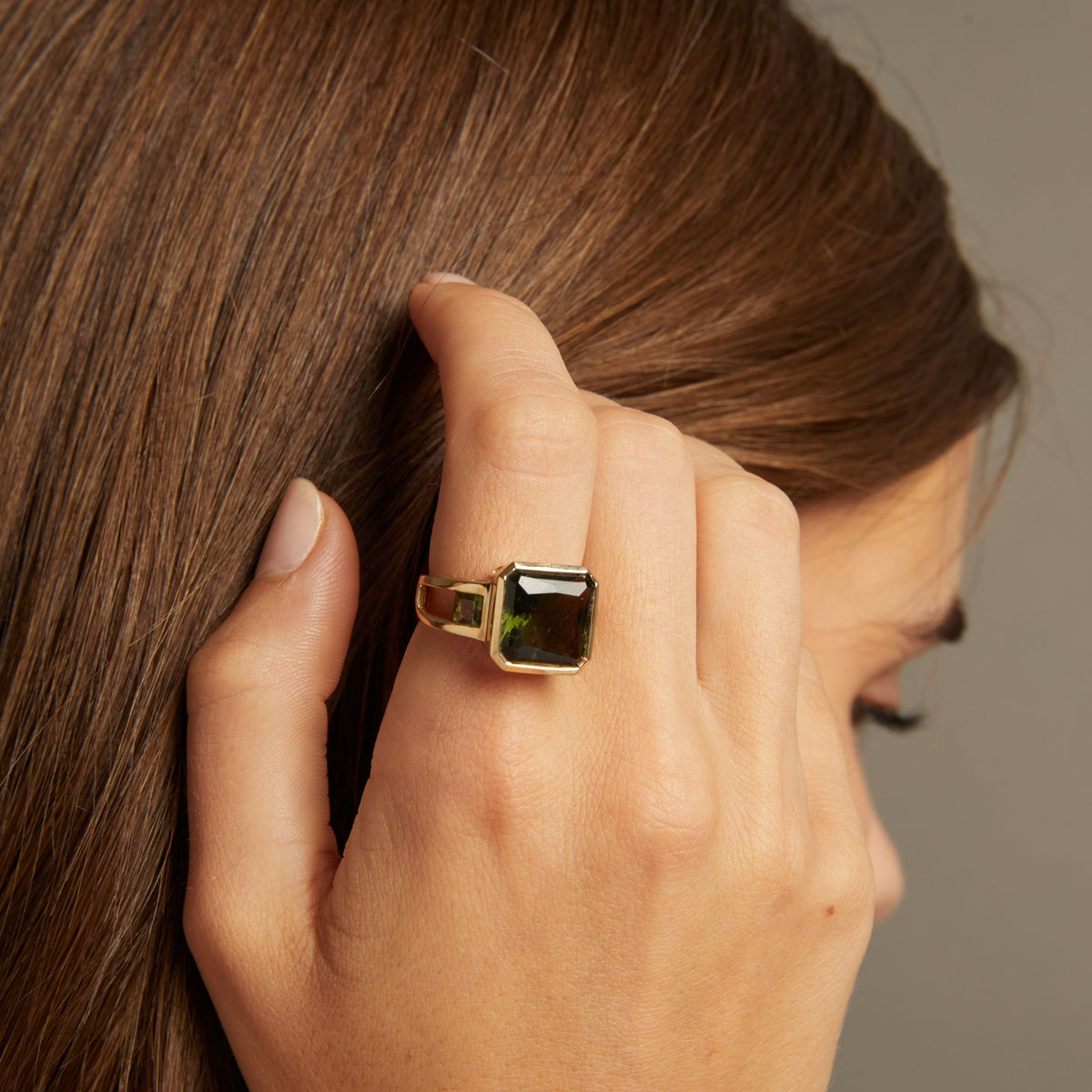 Model. Close up of woman wearing bold green ring on neutral background.