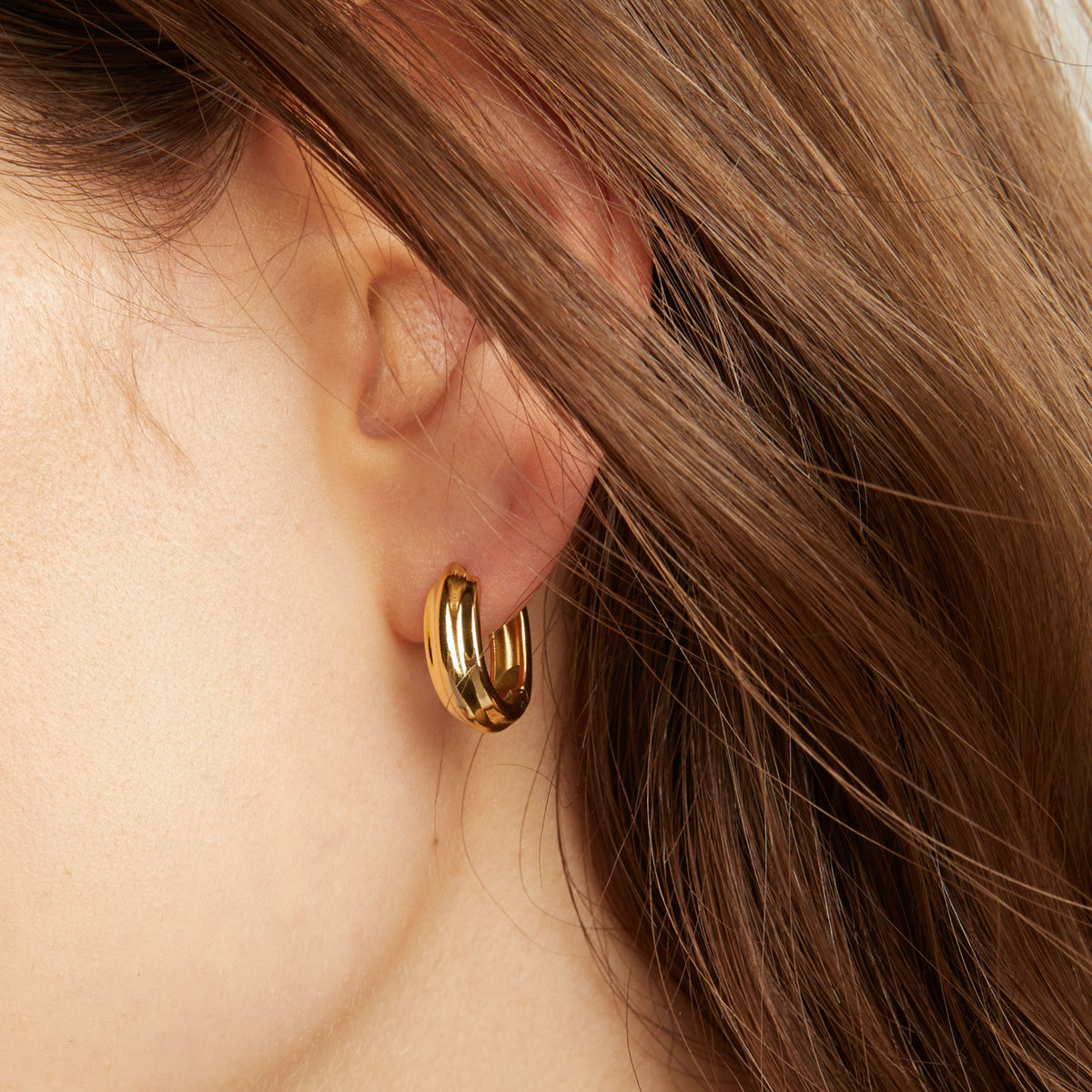 Close up of a person wearing gold hoop earrings.